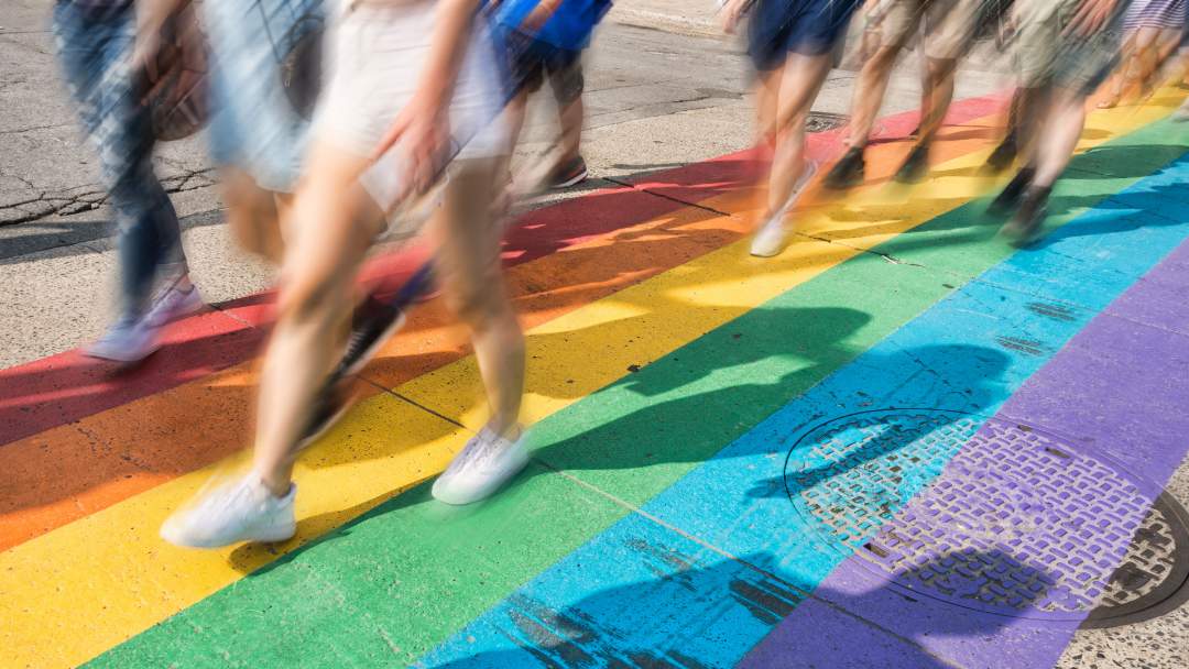 Personas que caminan por una calle con los colores del arcoíris durante el Mes del Orgullo