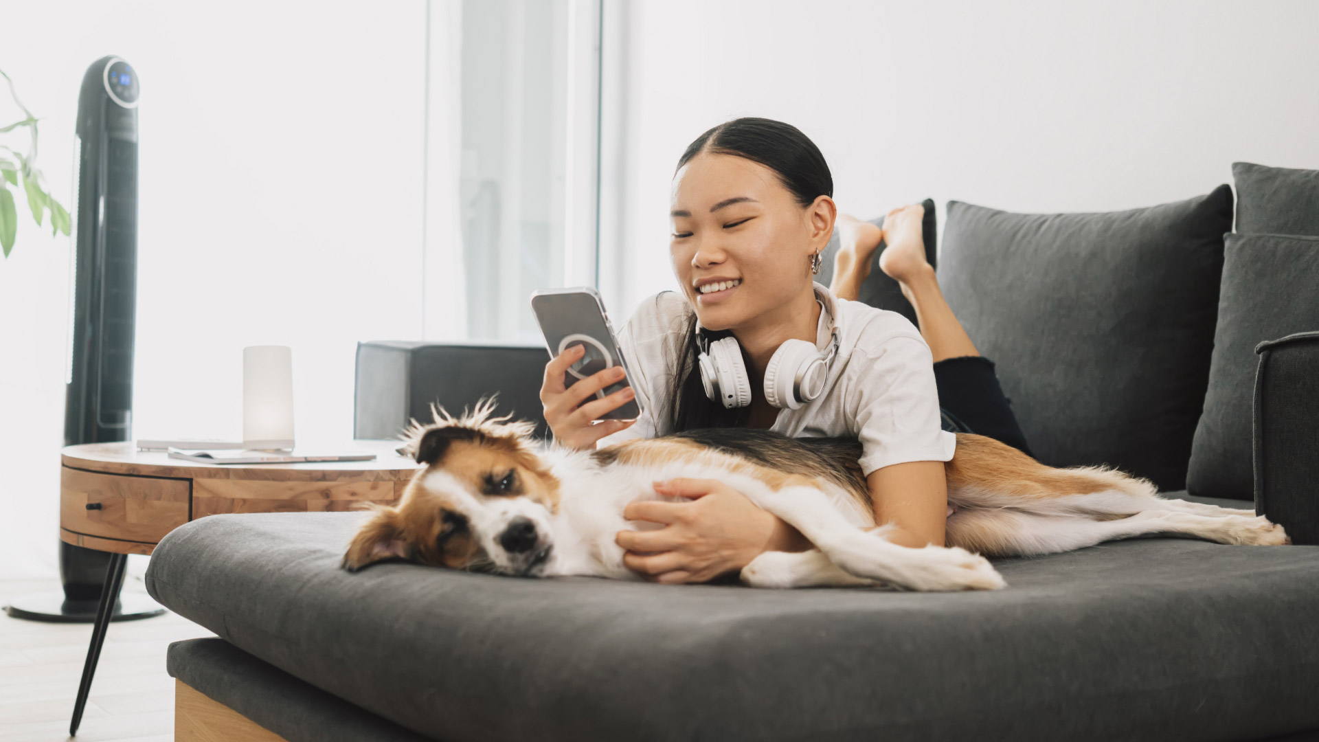 Una mujer con su teléfono descansa en un sofá con su perro