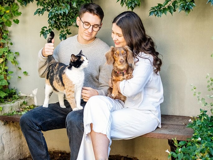 Un hombre y una mujer sentados juntos sosteniendo a un gato y a un perro